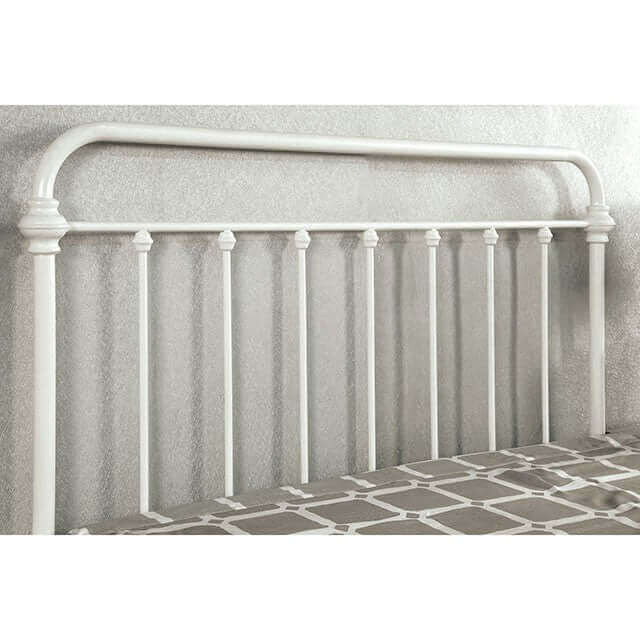 White metal bed headboard featuring seven spindles in a vintage powder-coated finish against a textured wall.