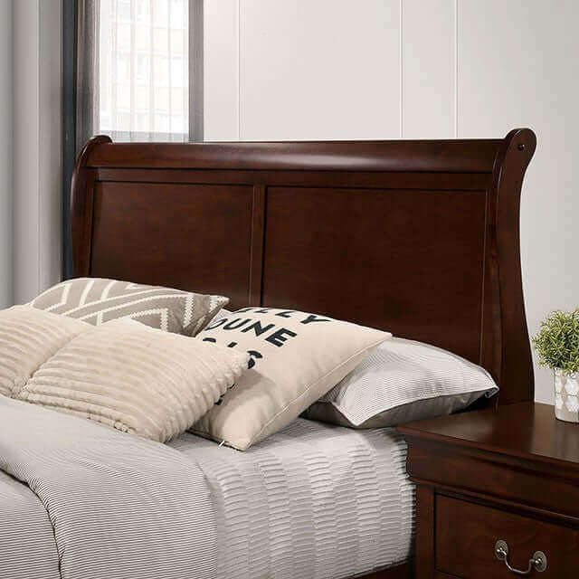 Louis Philippe cherry sleigh bed headboard with decorative pillows and gray bedding in a stylish bedroom setting.