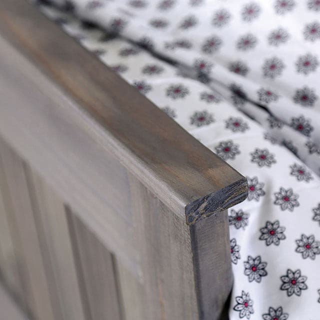 Close-up of the Rockwall brushed gray panel bed showcasing its weathered finish and floral patterned bedding.