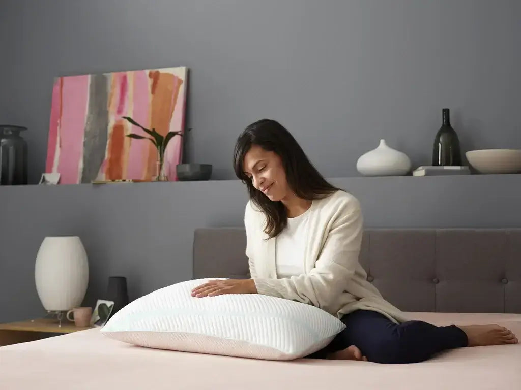 Woman touching the Tempur-Adapt ProLo + Cooling Pillow on a bed, showcasing its comfort and design.