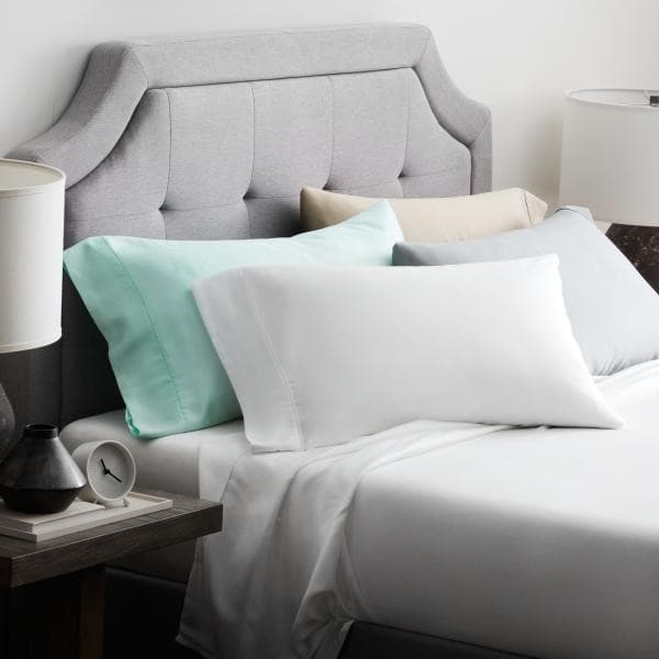 Cozy bed with Malouf Tencel™ Lyocell sheet set and colorful pillows, featuring a grey upholstered headboard.