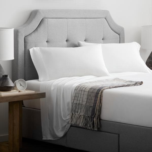 Stylish gray upholstered bed with white pillows and a cozy blanket, featuring bedside lamps and a wooden table.