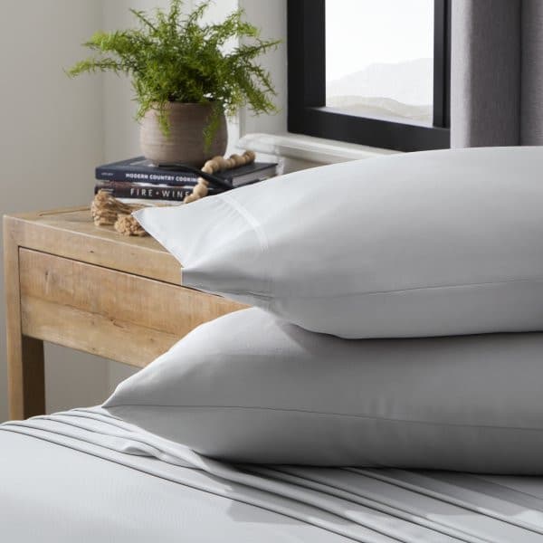 Soft gray Malouf bamboo rayon pillowcases resting on a neatly made bed beside a potted plant and books, showcasing comfort and style.