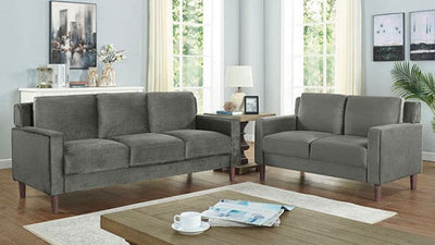 Contemporary gray flannelette loveseat and sofa set in a bright living room with large windows and wooden coffee table.