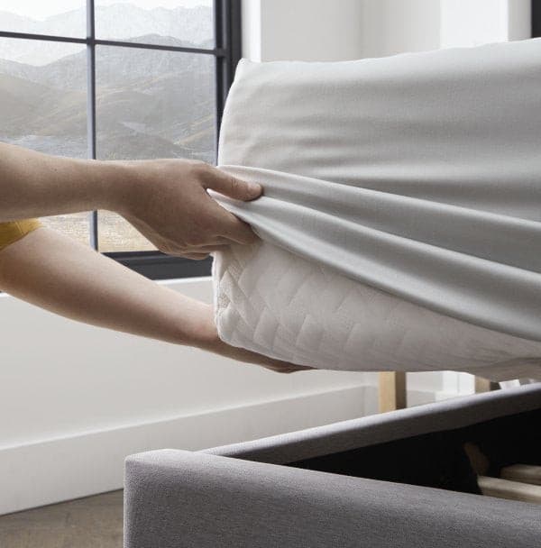 Person placing a smooth bamboo rayon sheet over a mattress in a modern bedroom setting.