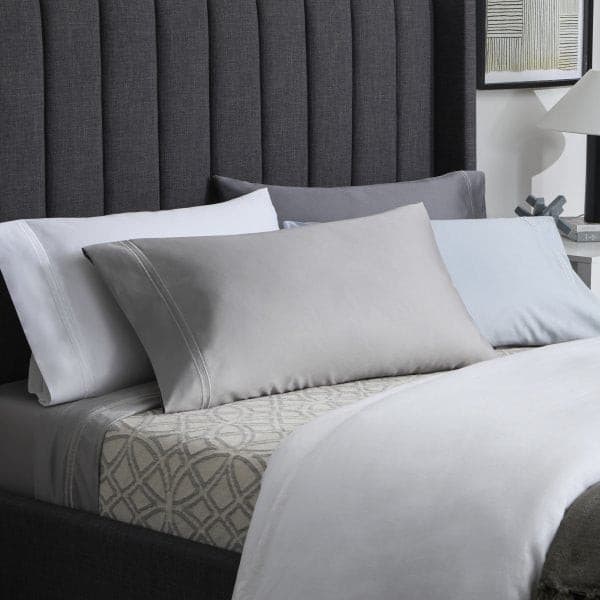 Elegant bedroom setup featuring Malouf Premium Smoke Supima® cotton sheets with various pillows against a dark headboard.