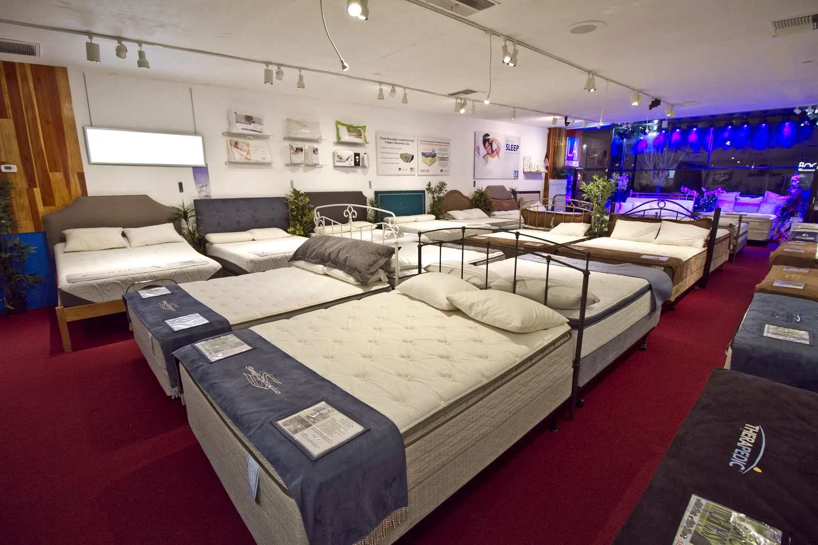 Rows of mattresses and headboards inside the Studio City showroom, with red carpet aisles and illuminated front windows