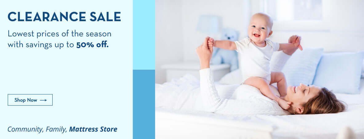 Mother playing with baby during clearance sale at mattress store, highlighting season's best prices and family community.