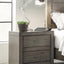 Modern Loft Collection Graystone Nightstand with lamp, plant, and digital tablet beside a bed, showcasing elegant design.