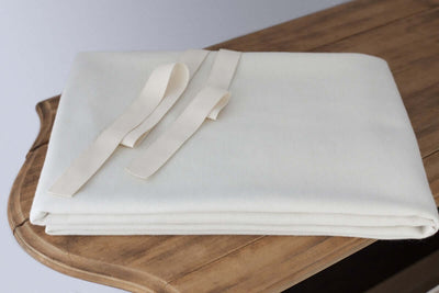 Organic natural wool mattress pad folded with cotton corner ties on a wooden table.