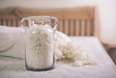 Glass jar filled with organic wool fiber on a bed, showcasing natural bedding materials for comfort.
