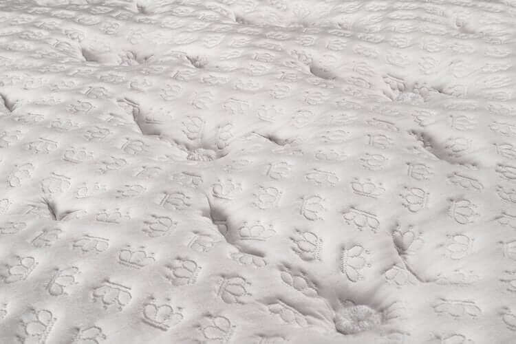 Close-up of a white quilted fabric featuring paw print and crown patterns, perfect for pet lovers or stylish bedding.