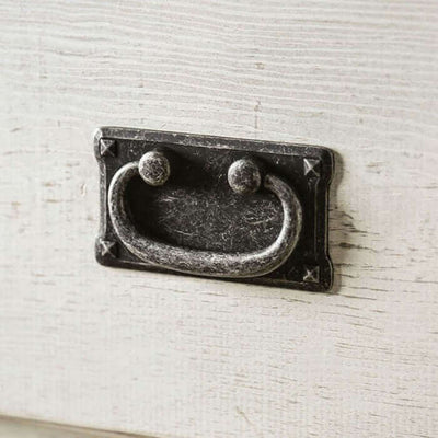 Close-up of decorative metal drawer pull on a weathered white dresser.