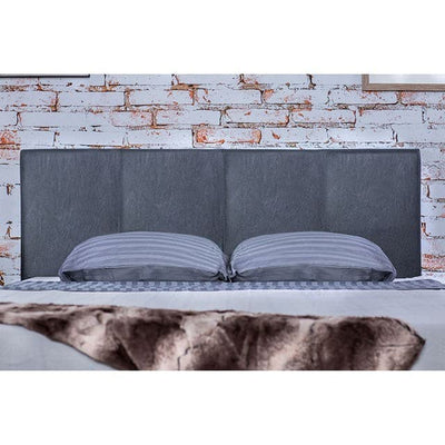 Modern gray padded headboard in a contemporary bedroom setting with striped pillows and a textured throw.